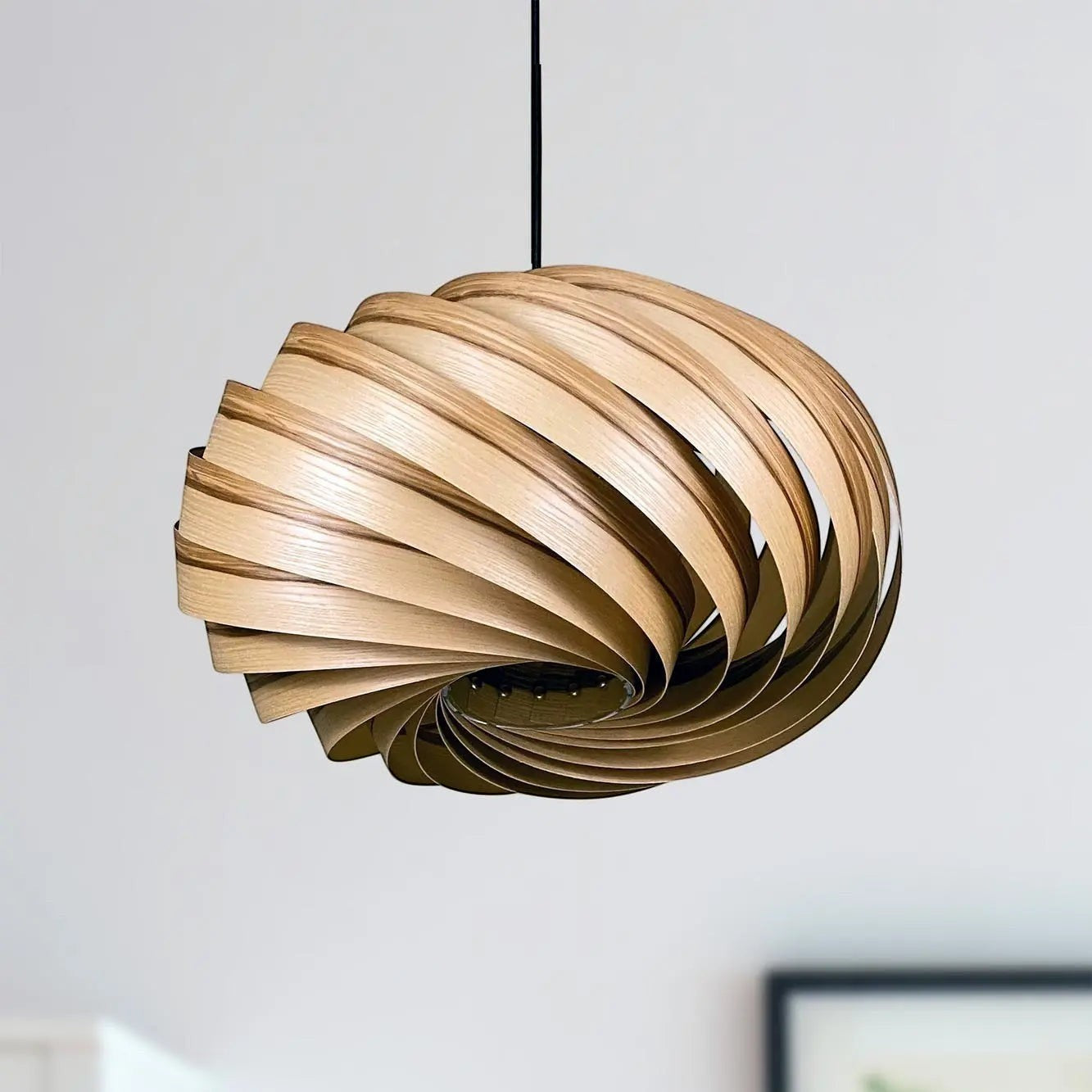 Gofurnit Quiescenta pendant lamp shade made of olive ash wood with a swirling, layered design. Natural wood tones.
