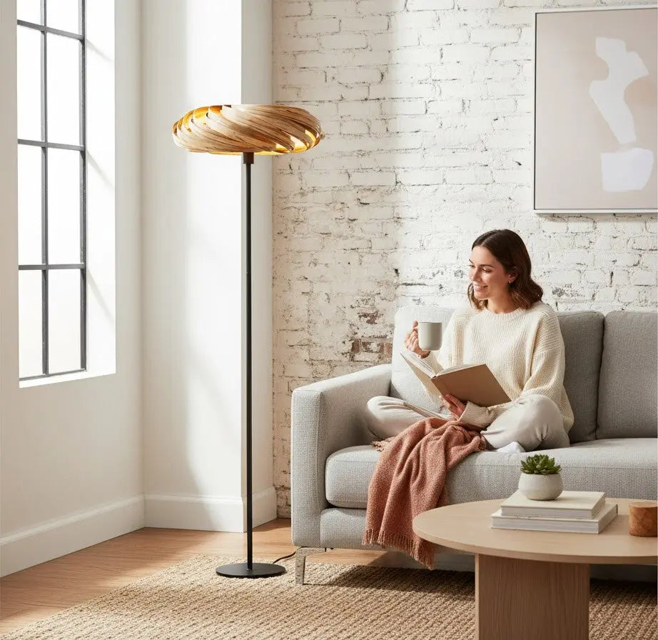 Gofurnit Veneria floor lamp with a swirling, layered amberwood shade and a black metal stand against a white brick wall.